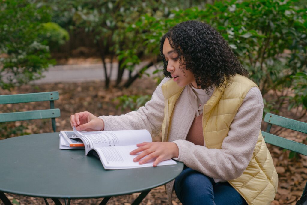 Student sitting outside at a table reading through a book